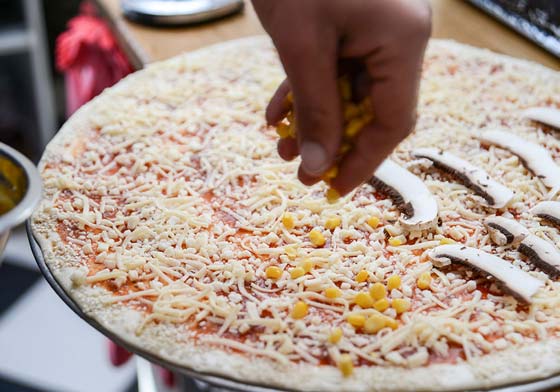 שלבי הכנת פיצה הנחת תוספות על פיצה משפחתית